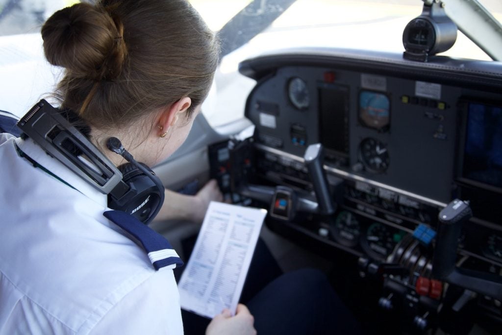 Female pilot in cockpit reviewing checklist.